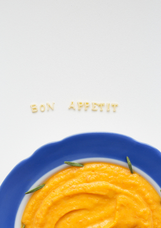 pumpkin soup in a blue plate on a napkin with flowers close-upの写真素材