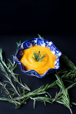 pumpkin soup in a blue plate on a black background with a branch of rosemaryの写真素材
