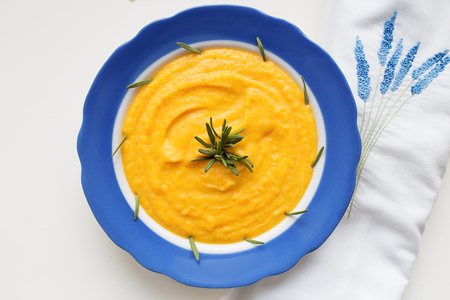 pumpkin soup in a blue plate on a napkin with flowersの写真素材