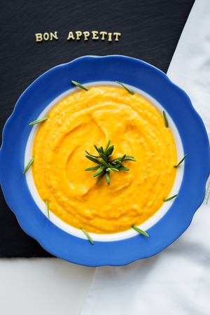 pumpkin soup in a blue plate on a black background with a white cloth, close-upの写真素材