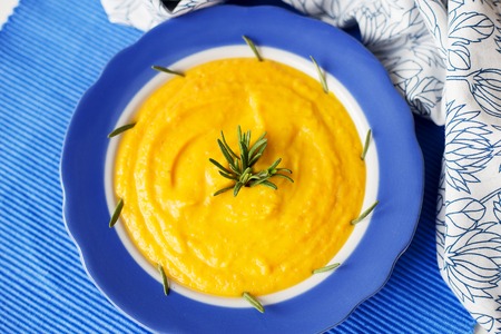 pumpkin cream soup in a blue plate on blue napkin with rosemaryの写真素材