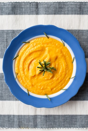 pumpkin cream soup in a blue striped plate on a napkin with rosemaryの写真素材