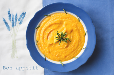pumpkin soup in a blue plate with rosemary on a napkin with flowersの写真素材