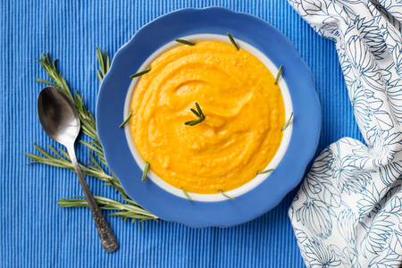 pumpkin cream soup in a blue plate on blue napkin, a branch of rosemaryの写真素材