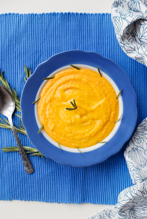 pumpkin cream soup in a blue plate on blue napkin, a branch of rosemaryの写真素材