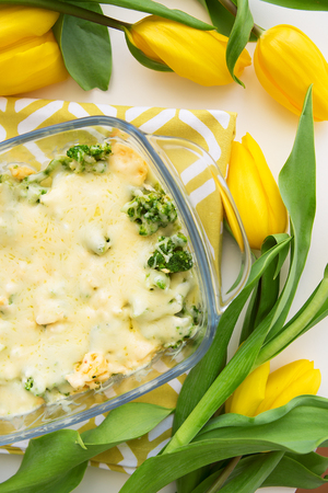 tasty casserole with broccoli, cheese and cream on a background of yellow tulipsの写真素材
