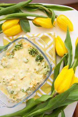 tasty casserole with broccoli, cheese and cream on a background of yellow tulips, close-upの写真素材