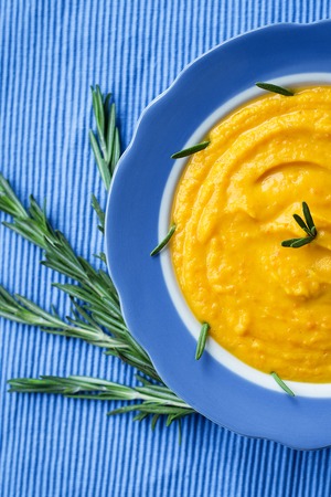 pumpkin cream soup in a blue plate on blue napkin, a branch of rosemaryの写真素材