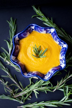 pumpkin soup on a black background with the sprigs of rosemary, close-upの写真素材
