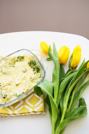 casserole with broccoli, cheese and cream on a background of yellow tulipsの写真素材