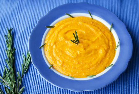 pumpkin cream soup in a blue plate on blue napkin, a branch of rosemaryの写真素材