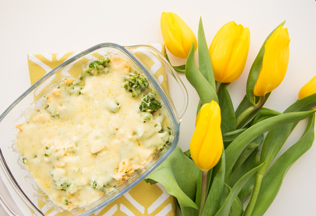 tasty casserole with broccoli, cheese and cream on a background of yellow tulipsの写真素材