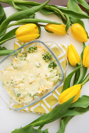 tasty casserole with broccoli, cheese and cream on a background of yellow tulips, close-upの写真素材