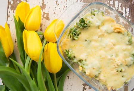 tasty casserole with broccoli, cheese and cream on a background of yellow tulips, close-upの写真素材