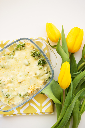 tasty casserole with broccoli, cheese and cream on a background of yellow tulipsの写真素材