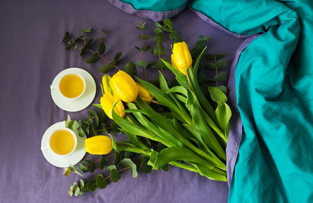 Yellow tulips and two cups of tea in bed, morningの写真素材