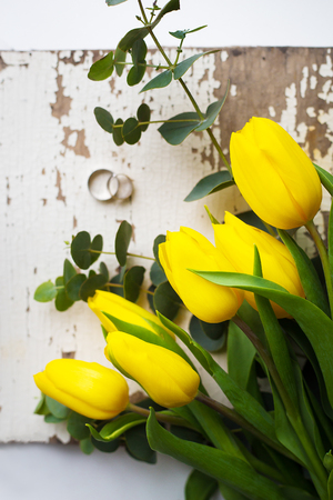 Beautiful wedding rings with yellow tulips on old white tableの写真素材