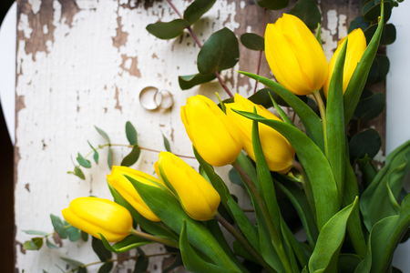 Beautiful wedding rings with yellow tulips on old white tableの写真素材
