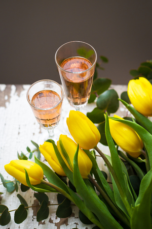 yellow tulips on a white table with glasses of rose wineの写真素材