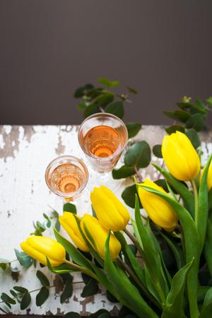 yellow tulips on a white table with a glass of rose wine, close-upの写真素材