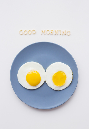two eggs on a plate and a yellow napkin, inscription Good Morningの写真素材