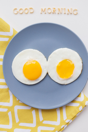 two eggs on a plate and a yellow napkin, inscription Good Morningの写真素材