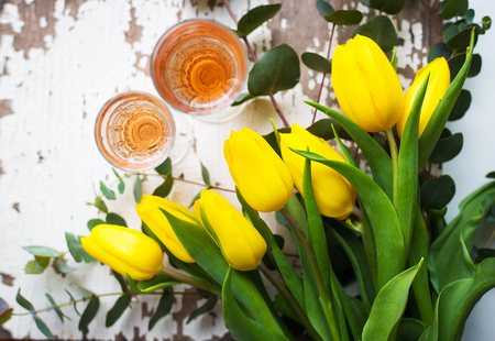 yellow tulips on a white table with glasses of rose wineの写真素材
