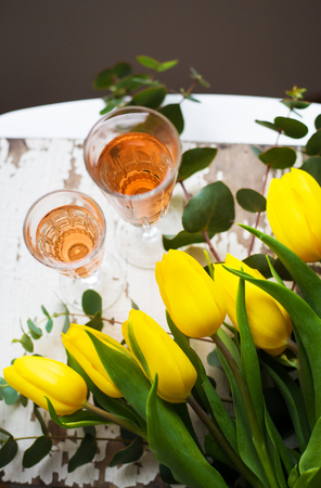 yellow tulips on a white table with glasses of rose wineの写真素材