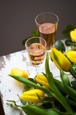 yellow tulips on a white table with a glass of rose wine, close-upの写真素材