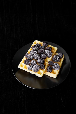 Belgian wafers with frozen blackberries on a black background.の写真素材