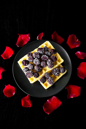 Belgian waffles with blackberries on a black background with petals of roses.の写真素材