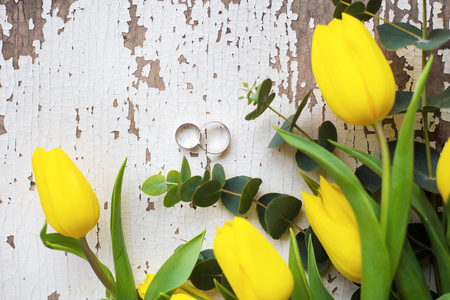 wedding rings with yellow tulips on old white tableの写真素材