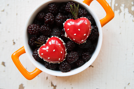 A full blackberry plate with a dessert in the form of a heart stands on a wooden background, close-up.の写真素材