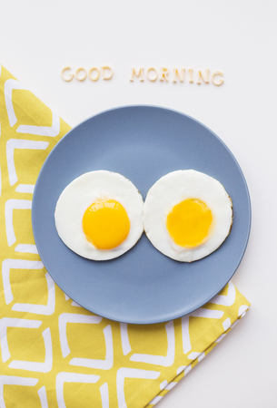 two eggs on a plate and a yellow napkin, inscription Good Morningの写真素材