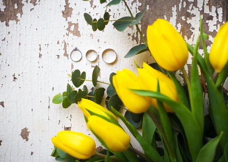 wedding rings with yellow tulips on old white tableの写真素材