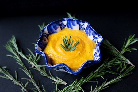 pumpkin soup in a blue plate on a black background with a branch of rosemaryの写真素材