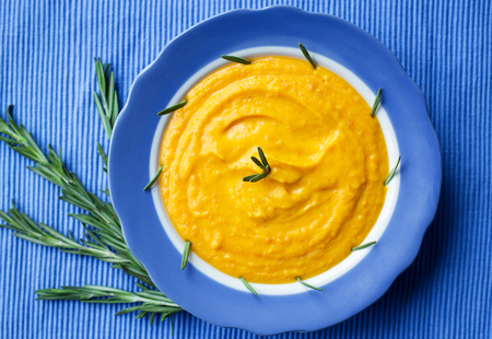 pumpkin cream soup in a blue plate on blue napkin, a branch of rosemaryの写真素材