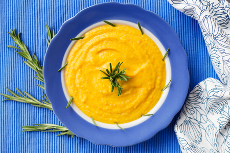 pumpkin cream soup in a blue plate on blue napkin, close-upの写真素材