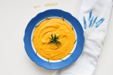 pumpkin soup in a blue plate on a napkin with flowersの写真素材