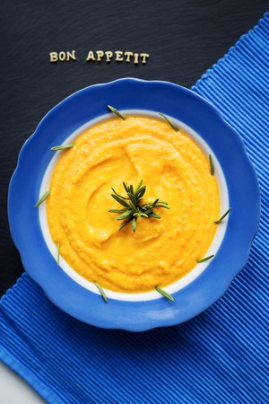 pumpkin soup in a blue plate on a black background with a blue cloth, close-upの写真素材