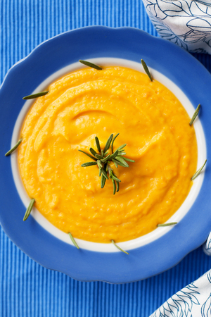 pumpkin cream soup in a blue plate on blue napkin with rosemaryの写真素材