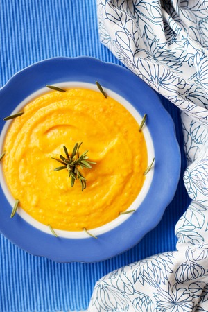 pumpkin cream soup in a blue plate on blue napkin with rosemaryの写真素材