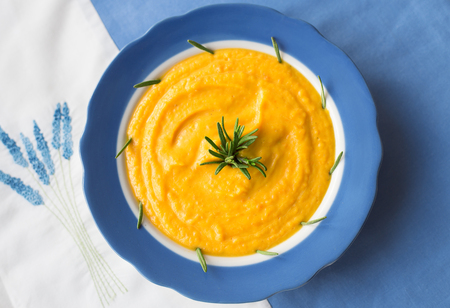 pumpkin soup in a blue plate with rosemary on a napkin with flowersの写真素材
