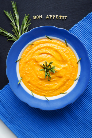 pumpkin soup in a blue plate on a black background with a blue napkinの写真素材