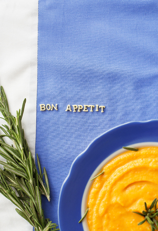 pumpkin soup in a blue plate with rosemary on a napkin with flowersの写真素材