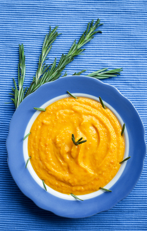 pumpkin cream soup in a blue plate on blue napkin, a branch of rosemaryの写真素材