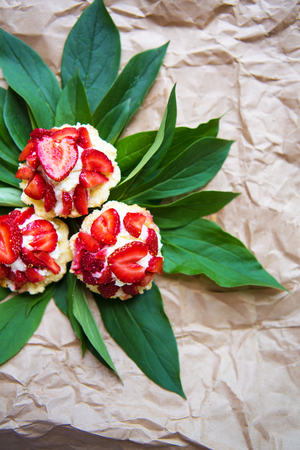 Beautiful and bright cupcakes with strawberries lie on green leaves, close-up.の写真素材