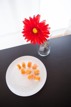Sushi roll with salmon, philadelphia on a white plate. Red flower in a vaseの写真素材