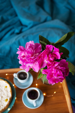 Coffee, pink peonies, cheesecake on a wooden tray, top view.の写真素材