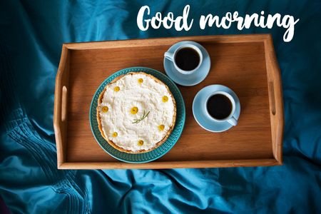 Two cups of coffee and cheesecake stand on a wooden tray, the inscription good morning.の写真素材